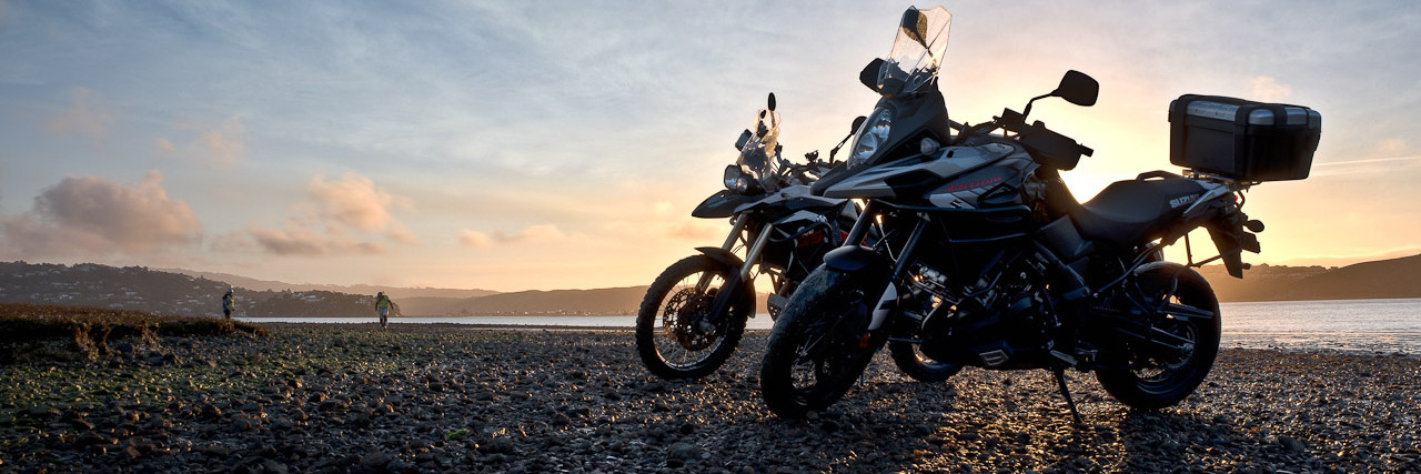 Two bikes parked on rocky seashore with sunset behind