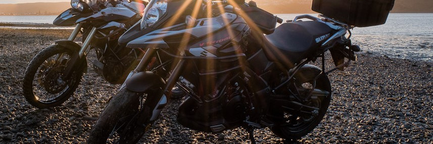 Two motorbikes on rocky sea front wiht sunset